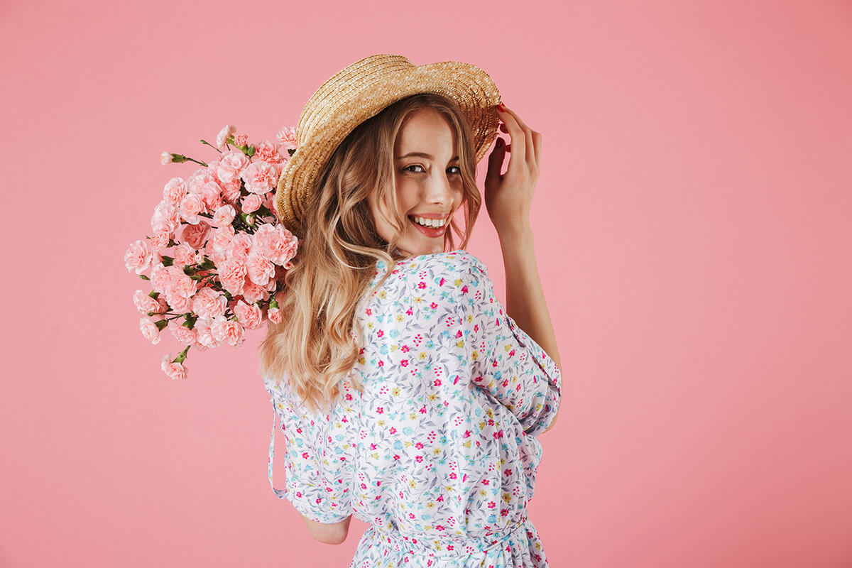 Frau in blauem Sommerkleid mit Strohhut und rosanem Blumenstrauß